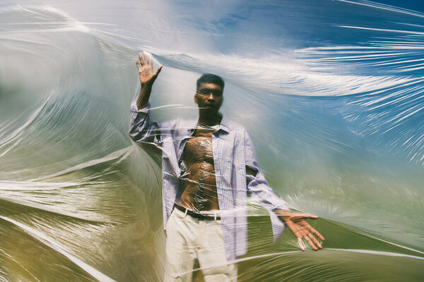 trendy african american man posing near cellophane film outdoors