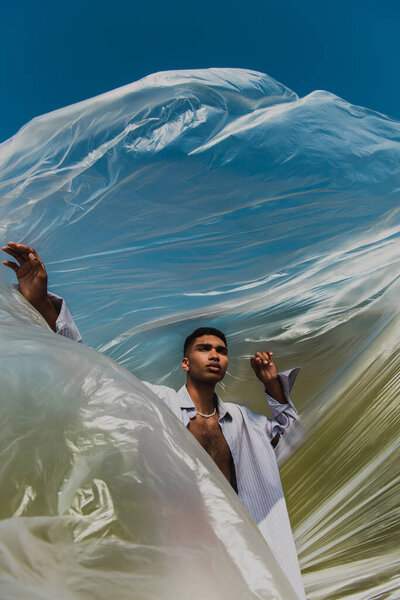 stylish african american man near cellophane film under blue sky