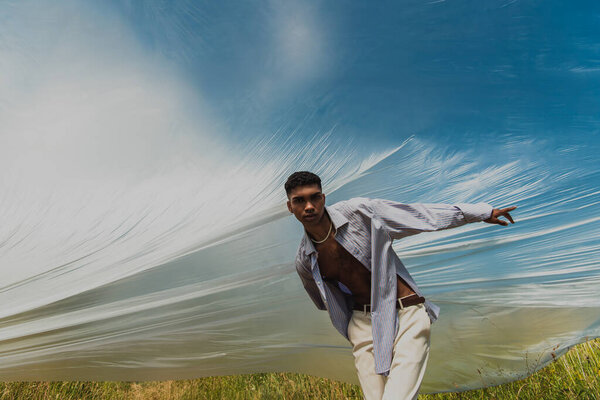 african american man in trendy clothes pointing with finger under cellophane film in field