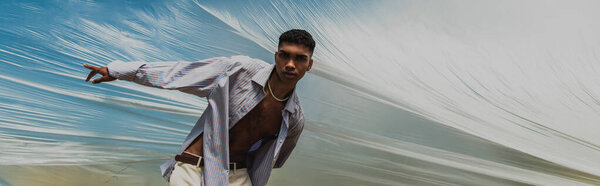 fashionable african american man looking at camera and pointing with finger under polyethylene, banner