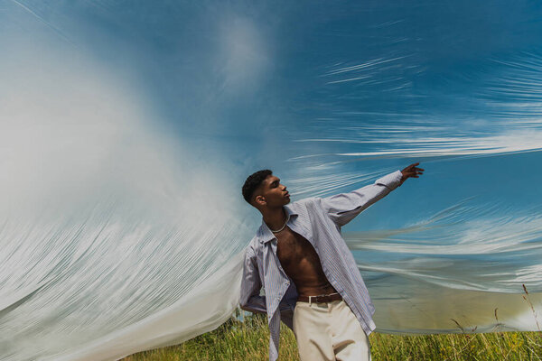 fashionable african american man with outstretched hand posing near polyethylene film in field