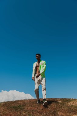 full length african american man in trendy clothes walking in meadow