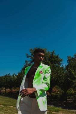 young african american man in fashionable blazer near green trees 