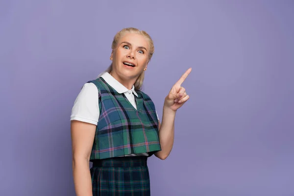 Amazed blonde student pointing with finger isolated on purple