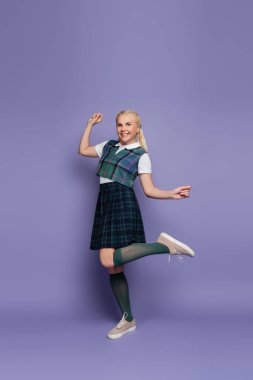 Full length of smiling student in uniform standing on purple background 