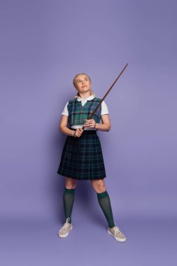 Full length of student in uniform holding pointer on purple background 