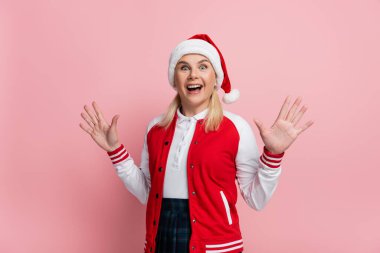 Excited woman in santa hat looking at camera isolated on pink 