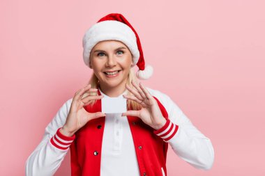 Cheerful woman in santa hat holding empty driving license isolated on pink 
