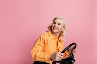 Positive driver holding steering wheel and looking away isolated on pink 