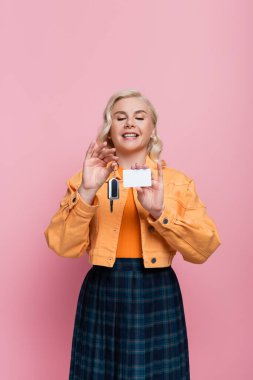 Happy driver holding car key and empty driving license isolated on pink 