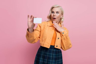 Shocked blonde woman holding empty driving license isolated on pink 