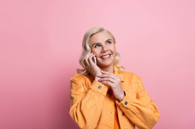 Happy blonde woman talking on mobile phone isolated on pink 