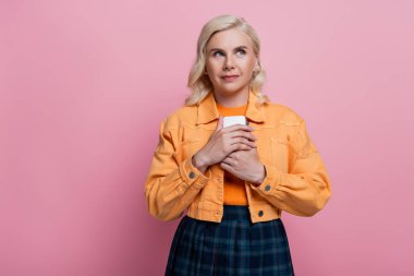Dreamy woman in orange jacket holding smartphone isolated on pink 