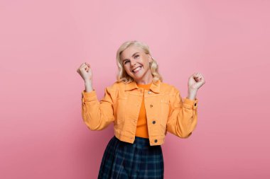 Cheerful blonde woman showing yes gesture isolated on pink 