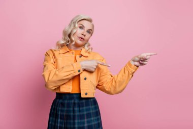 Blonde woman in jacket pointing with fingers isolated on pink 