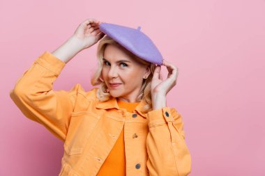 Stylish blonde woman holding beret isolated on pink 