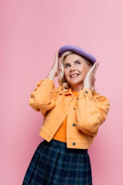 Happy woman in jacket adjusting beret isolated on pink 