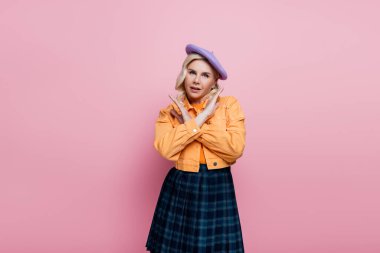 Stylish woman in beret showing stop sign at camera isolated on pink 