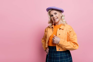 Stylish woman in beret holding hand on hip on pink background