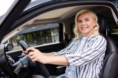 Cheerful woman looking at camera while sitting in car during driving course 