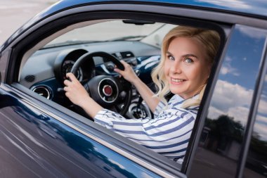 Blonde woman looking at camera in blurred car during driving course 