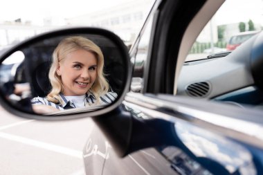 Positive woman reflecting in blurred car mirror  clipart
