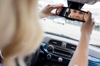 Smiling blonde driver adjusting mirror in car 