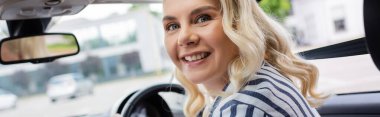 Blonde beginner looking at camera on driving course in auto, banner 
