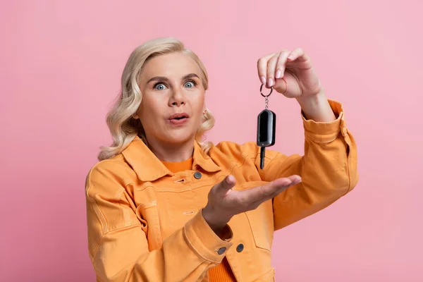 Astonished driver pointing at car key isolated on pink