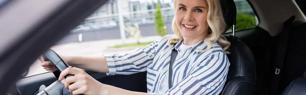 Happy blonde driver looking at camera during driving course in car, banner