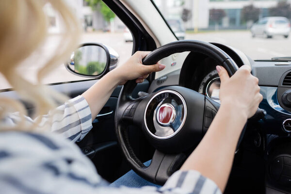 Cropped view of blonde driver holding steering wheel of car 