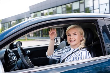Happy blonde woman holding key on driver seat in car 