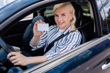 Happy driver holding license and looking at camera in auto 