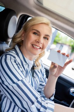 Cheerful woman holding empty driver license in car 