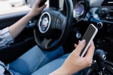 Cropped view of blurred driver using mobile phone with blank screen in car 