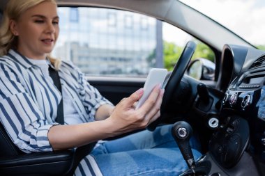 Blurred woman using smartphone on driver seat in auto 