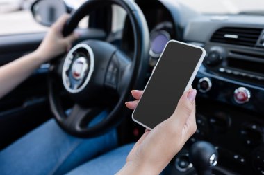 Cropped view of blurred woman holding smartphone with blank screen in blurred car 