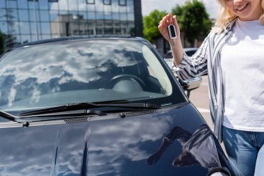 Cropped view of smiling woman holding key near car outdoors 