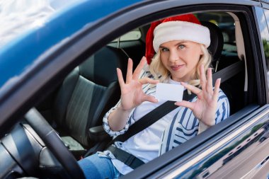Blonde woman in santa hat holding driver license in auto 