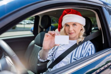 Blonde woman in red santa hat holding driving license in auto 
