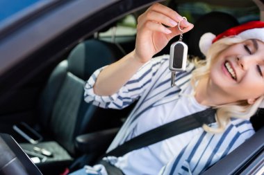 Blurred cheerful woman in santa hat holding key in car 