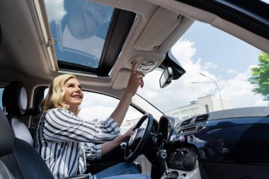 Positive blonde woman pushing button and looking at top of car 