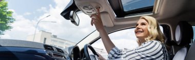 Cheerful driver pushing button and looking at window on top of car, banner 