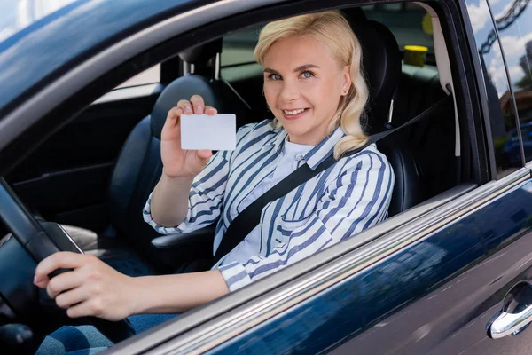 Happy driver holding license and looking at camera in auto