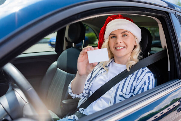 Cheerful driver in santa hat holding license in auto 