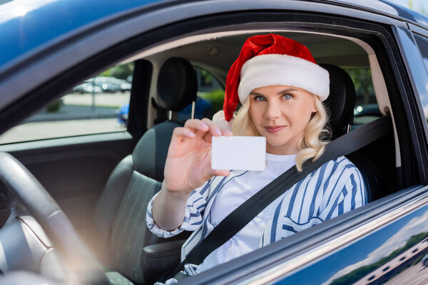 Blonde woman in red santa hat holding driving license in auto 