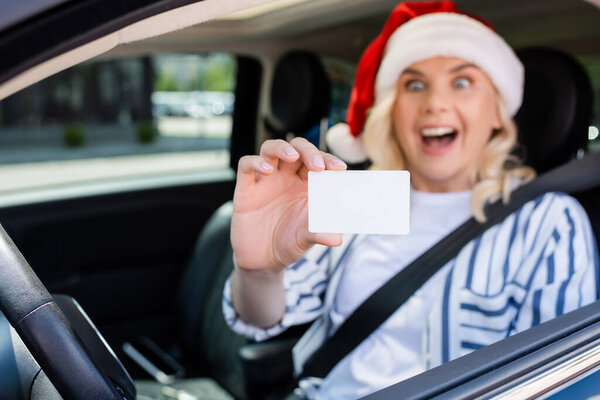 Blurred excited woman in santa hat holding driving license in car 