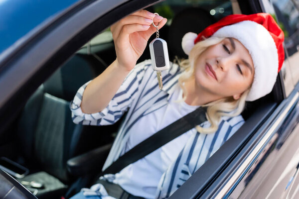 Blurred woman in santa hat holding key while sitting in car 