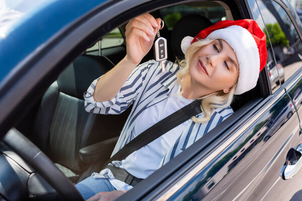 Blonde driver in santa hat holding key on seat in car 