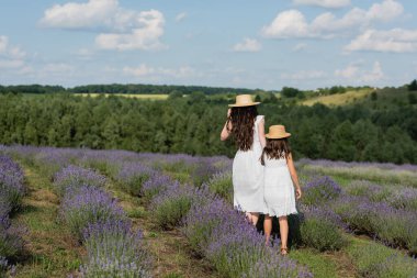 back view of mother and daughter in white dresses walking in lavender field